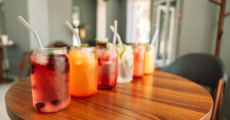 Fruit drinks with berries and ice in glass glasses and straws on a wooden table.
