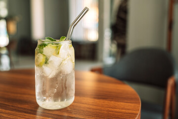 Lemonade with ice in a glass glass and a straw on a wooden table.