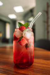 Lemonade with berries and ice in a glass glass and a straw on a wooden table.
