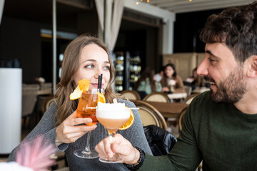 Couple toasting with cocktails in a cozy bar. They are smiling and enjoying their time together in a stylish indoor setting with a warm atmosphere.