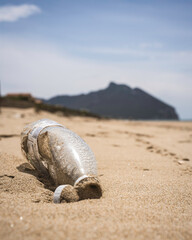 Plastic bottle discarded on sandy beach with distant mountains. Environmental impact of plastic waste on coastal areas. Focus on sustainability and pollution awareness efforts.