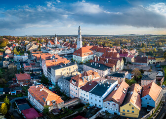 Stunning aerial view of Gryfów Śląski, Poland, during autumn, capturing the historic town center with its charming red-tiled roofs, church steeples, and surrounding colorful foliage.