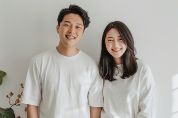 Obraz premium Portrait of a content asian couple in their 20s showing off a lightweight base layer isolated in bare monochromatic room