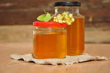 linden honey in a glass jar and linden flower on the table in the sunlight. selective focus