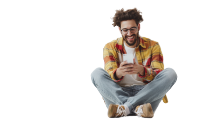 Joyful man sitting on a white floor, captivated by his phone, against a transparent backdrop.