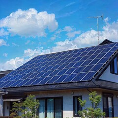Naklejka premium Modern house with a large array of solar panels on the roof under a bright blue sky with clouds, showcasing renewable energy and eco-friendly living.