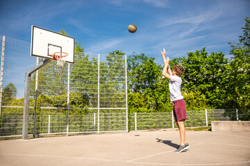 Young basketball player practicing alone in the urban basketball court with trees on background