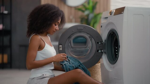 African American girl ethnic lady biracial woman housewife home laundry clothes open washing machine housekeeping take clean wet jeans pants find mobile phone in pocket broken smartphone shock upset