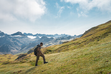 Young man is walking up a grassy hill in the mountains under a cloudy sky, surrounded by lush greenery with a vast landscape spreading in the horizon. High quality photo