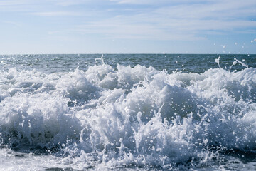 Sea wave close-up, water splash in the sea, sea foam against the sky on a summer sunny day