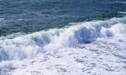 Sea wave close-up, splash of water in the sea, sea foam on a summer sunny day. Blue sea texture with waves