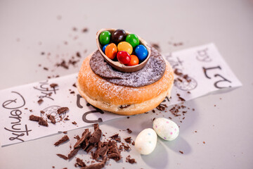 Donuts recheado encima da mesa com raspas de chocolate decorado com ovinhos de páscoa e meio ovo de chocolate branco e preto recheado com chocolate coloridos