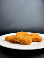 Deep fried crispy and delicious chicken nugget dish on white plate. Food photography isolated on vertical dark black background with empty copy space for text.