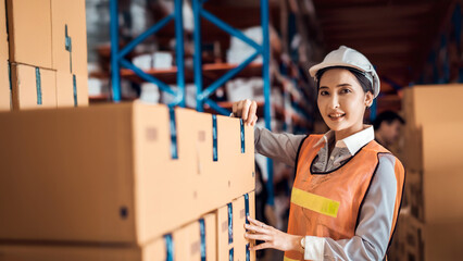 Asian woman wearing a hardhat standing cargo at goods warehouse and check packaging for control...