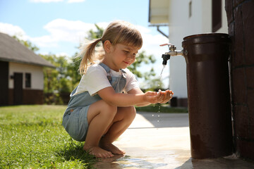 Water scarcity. Cute little girl drawing water with hands from tap outdoors