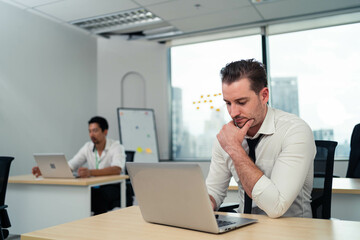 Obraz premium A man is sitting at a desk with a laptop open in front of him. He is wearing a black tie and he is in a state of distress