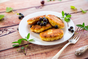 Fried curd cheese pancakes with black currants, on a wooden table