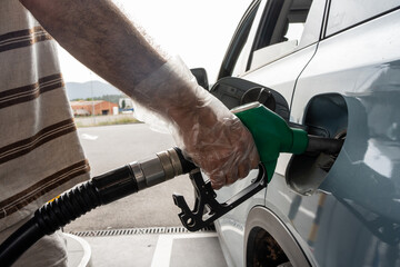 man's hand with plastic gloves pouring petrol into a light blue car