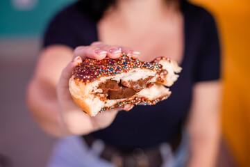 Donuts rasgado ao meio com recheio de chocolate e coberto com confetes sendo segurado por mão...