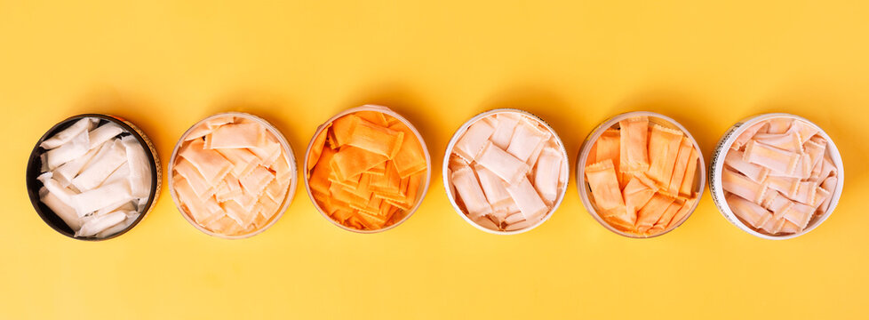 Multi-colored snus sachets with different flavors are placed in jars on a yellow background.
