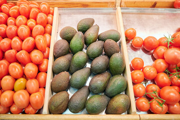 Avocados and two varieties of tomatoes for sale in a display case in the fruit and vegetable...