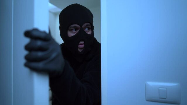 Close-up of a male thief with black mask opening the door to enter the room of apartment, home security to prevent the crimination, criminal impact on economic society.
