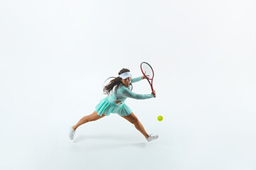Female tennis player in light blue outfit performs powerful forehand in motion against white studio background. Concept of professional sport, championship, active lifestyle, tournament. Ad