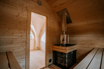  Interior of a wooden sauna with a stove and open door leading to a bright room. Warm, inviting, and relaxing atmosphere.