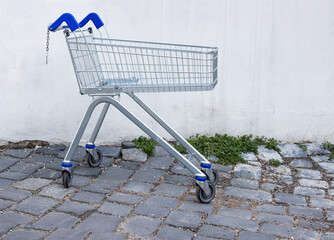 Abandoned empty shopping metal cart with blue grip standing  in the store backyard by dirty...