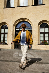 Stylish young man with red hair walking in front of an elegant building.