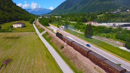 Steam train immersed in the Trentino landscape. old technology that recalls the transport and times of the past, a dive into the past. Romantic video of the locomotive with carriages made with a drone