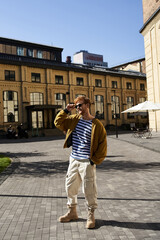 Red-haired man in debonair attire stands in front of building.