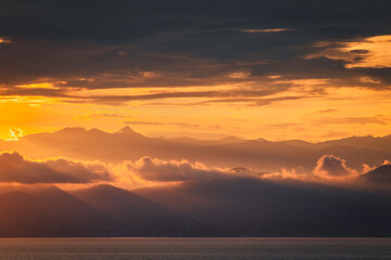 The photo captures a breathtaking golden sunset over majestic mountains. The sky is ablaze with hues of orange, pink, and gold, casting a warm glow on the rugged peaks. =