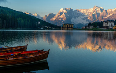 Lake Misurina in Dolomites, Dolomiti mountain, Italian Alps, Belluno, Italy. Alpine lake with reflection at sunrise and wooden boats tied to the dock at the lake. Summer vacation destination