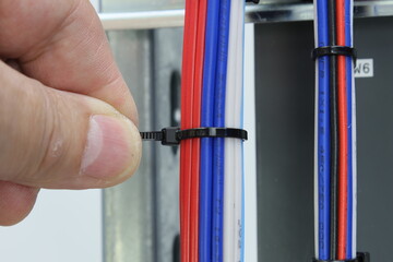 Installation of a cable tie on an insulated mounting wire in an electrical panel. Close-up. 