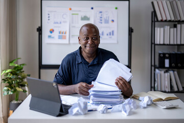 A man is sitting at a desk with a pile of papers in front of him
