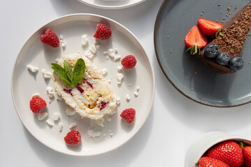 Plates with desserts close-up on a white background. Copy space. Pecan pie, meringue roll and chocolate cake are decorated with berries and mint leaves. Breakfast and tea