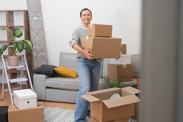 Enthusiastic woman rejoices in moving to modern housing holding cardboard boxes of different sizes...