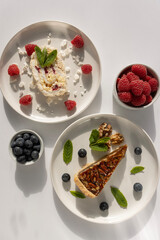 Plates with desserts close-up on a white background. Copy space. Pecan pie, meringue roll and chocolate cake are decorated with berries and mint leaves. Breakfast and tea