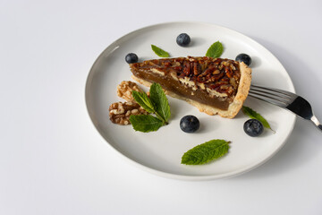 Pecan pie on a plate. Blueberries, nuts and mint leaves for dessert decoration. A yellow plate on a white background close-up.