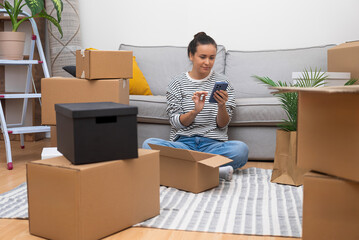 Woman scrolls social media in smartphone with carton boxes around near sofa in house waits for...