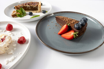 A piece of chocolate cake on a plate is decorated with berries. Dessert on a white background. Copy space, close-up.Fork on a plate