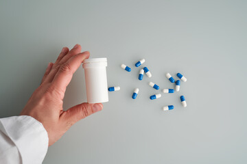 A hand holds a jar of white and blue pill on a blue background.