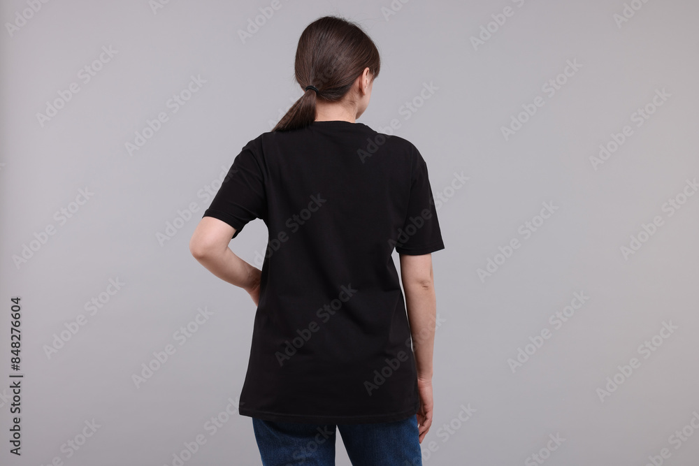 Wall mural Woman in stylish black t-shirt light grey on background, back view