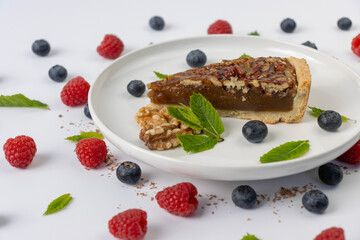 Pecan pie on a plate. Blueberries, nuts and mint leaves for dessert decoration. A yellow plate on a white background close-up.