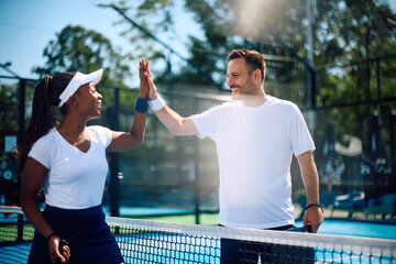 Happy athletic couple giving high five while playing paddle tennis on  court.