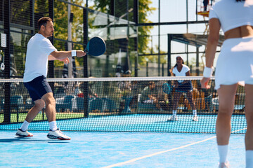 Athletic man in action during paddle tennis match in mixed doubles.