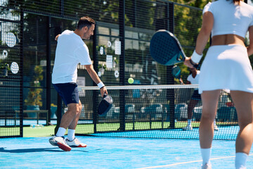 Obraz premium Paddle tennis player hitting ball while playing match with friends on outdoor court.