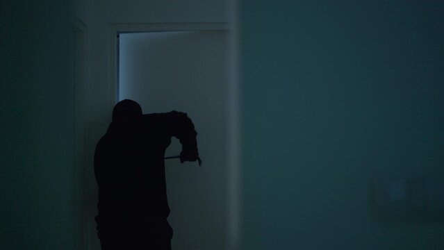 Rear view of the creepy burglar with black mask breaking the door for robbery the apartment, home security to prevent the crimination, criminal impact on economic society.
