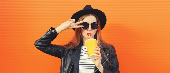 Portrait stylish young woman drinking juice posing in black rock style leather jacket, round hat
